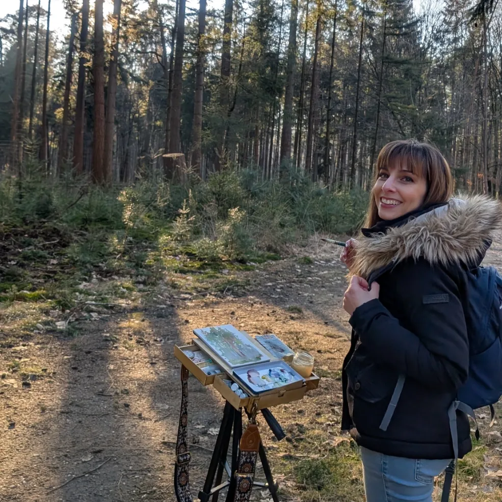 Maddy Bellwoar painting with gouache at a field easel in a pine forest